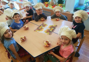 Dzieci przy stolikach prezentują wykonane owocowe desery.